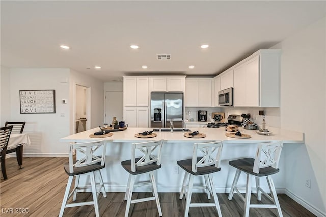 kitchen featuring stainless steel appliances, visible vents, light wood-style flooring, white cabinets, and a peninsula