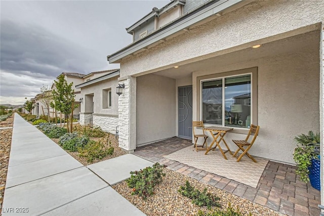 view of exterior entry with a patio, stone siding, and stucco siding