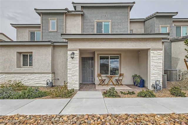 view of front of home with covered porch, stone siding, cooling unit, and stucco siding