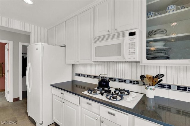 kitchen featuring dark countertops, decorative backsplash, white cabinets, light tile patterned flooring, and white appliances