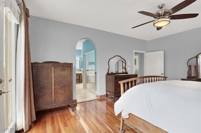 bedroom with arched walkways, ceiling fan, light wood finished floors, and ensuite bathroom