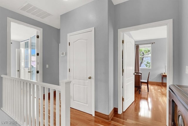 hall with light wood-style flooring, visible vents, and baseboards