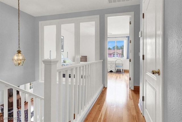 corridor featuring light wood finished floors, visible vents, and an upstairs landing