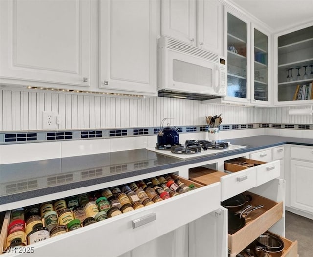 interior space featuring white appliances, dark countertops, glass insert cabinets, tile patterned floors, and white cabinetry