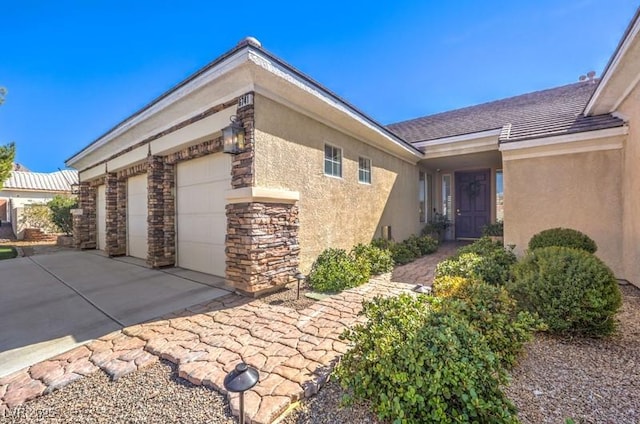 view of side of home featuring a garage, concrete driveway, stone siding, and stucco siding