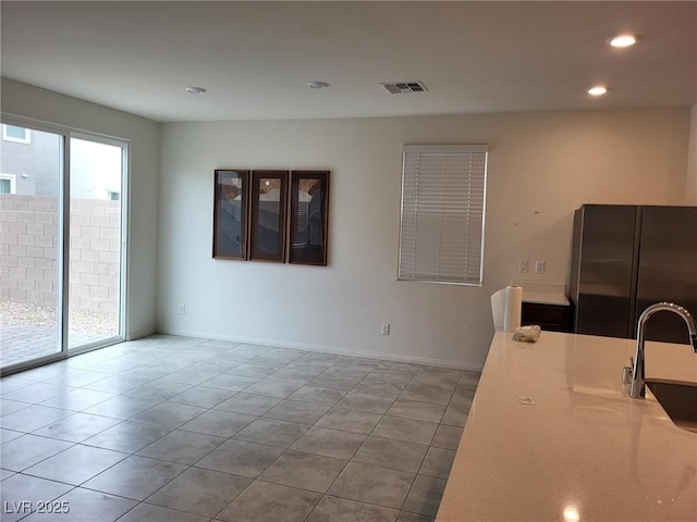 kitchen featuring a sink, visible vents, baseboards, freestanding refrigerator, and tile patterned floors