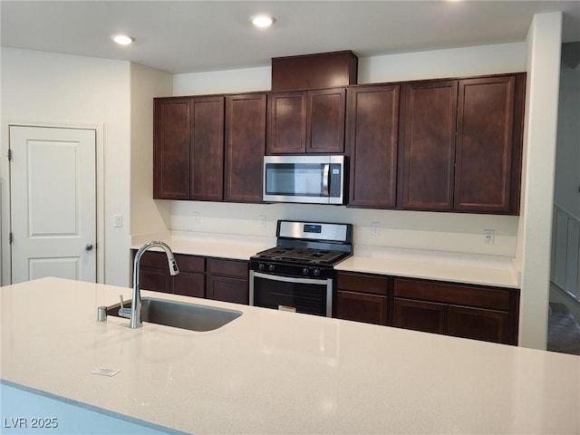 kitchen with appliances with stainless steel finishes, light countertops, dark brown cabinets, a sink, and recessed lighting