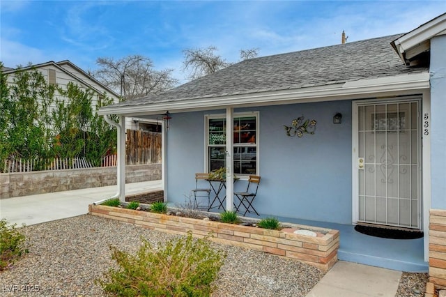 doorway to property featuring covered porch, roof with shingles, fence, and stucco siding