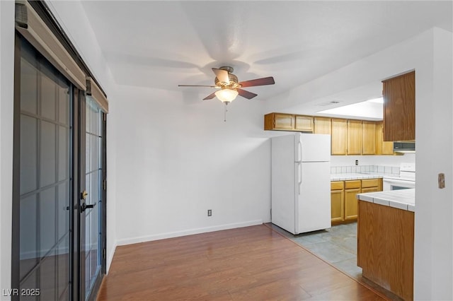 kitchen with range hood, tile counters, light wood-style floors, white appliances, and baseboards