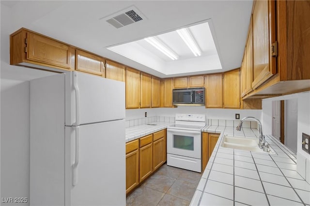 kitchen with light tile patterned floors, white appliances, a sink, visible vents, and tile counters