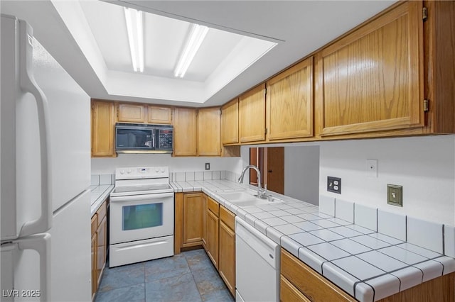 kitchen with a raised ceiling, white appliances, a sink, and tile counters