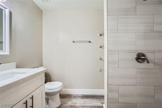 full bath featuring baseboards, tiled shower, toilet, wood finished floors, and vanity