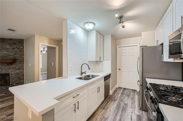 kitchen featuring visible vents, appliances with stainless steel finishes, a peninsula, white cabinetry, and a sink