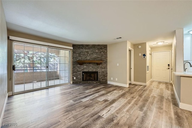 unfurnished living room with a stone fireplace, light wood finished floors, visible vents, and baseboards