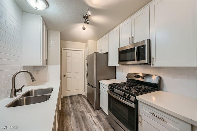 kitchen with decorative backsplash, appliances with stainless steel finishes, wood finished floors, white cabinetry, and a sink