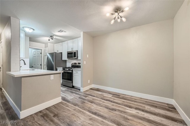 kitchen with stainless steel appliances, visible vents, white cabinets, a sink, and wood finished floors