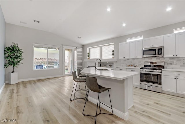 kitchen with stainless steel appliances, light countertops, decorative backsplash, a sink, and a kitchen bar