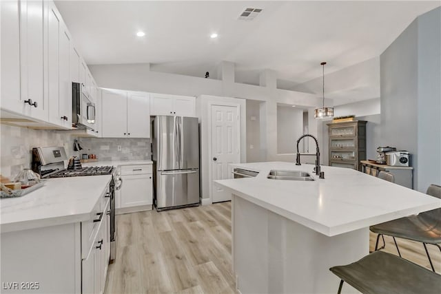 kitchen with lofted ceiling, stainless steel appliances, a sink, visible vents, and decorative backsplash