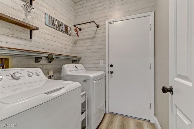 washroom featuring wooden walls, laundry area, light wood finished floors, and washing machine and clothes dryer