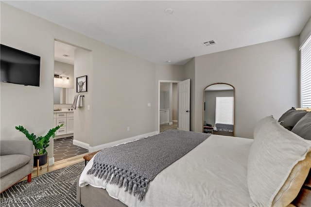 bedroom featuring connected bathroom, wood finished floors, visible vents, and baseboards