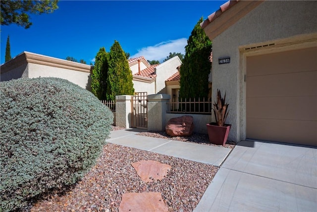 view of side of home with a garage, a tiled roof, a gate, fence, and stucco siding