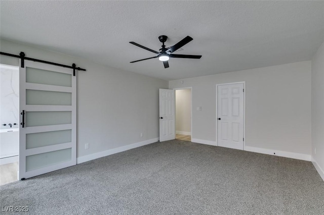 unfurnished bedroom featuring baseboards, ceiling fan, carpet, a barn door, and a textured ceiling