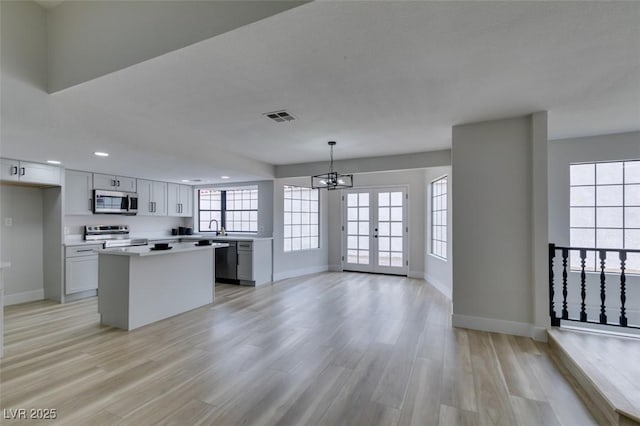 kitchen with visible vents, a kitchen island, light wood-style flooring, appliances with stainless steel finishes, and an inviting chandelier