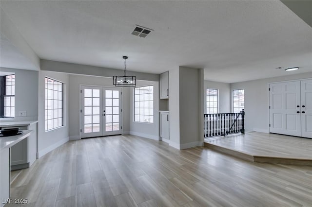 unfurnished dining area with visible vents, baseboards, light wood-type flooring, french doors, and an inviting chandelier