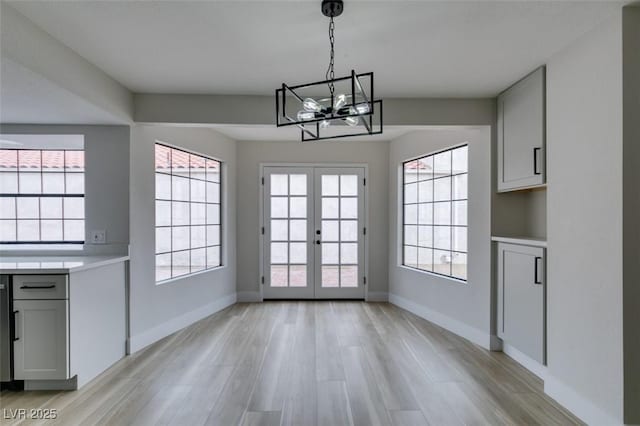 unfurnished dining area with a chandelier, light wood-style flooring, french doors, and baseboards