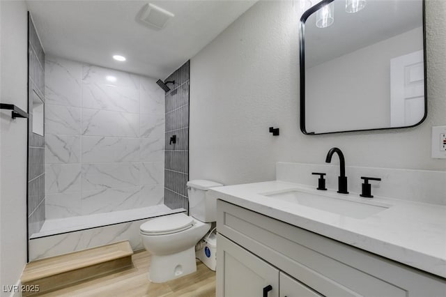 bathroom with toilet, wood finished floors, vanity, and a tile shower