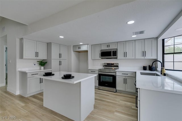 kitchen featuring visible vents, light wood-style flooring, a sink, stainless steel appliances, and light countertops