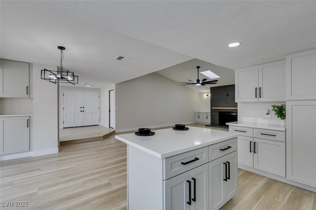 kitchen featuring visible vents, light countertops, ceiling fan with notable chandelier, light wood-type flooring, and a center island