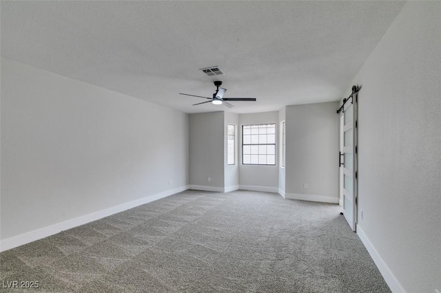 unfurnished room featuring visible vents, baseboards, light colored carpet, a barn door, and a textured ceiling