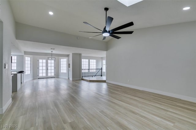 unfurnished living room featuring light wood finished floors, baseboards, lofted ceiling with skylight, recessed lighting, and a ceiling fan