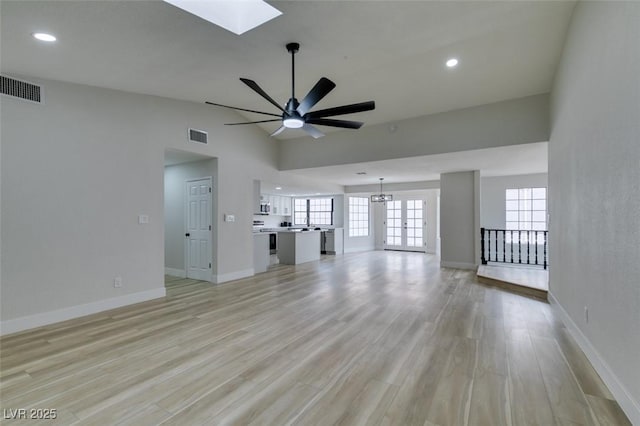 unfurnished living room with lofted ceiling with skylight, baseboards, visible vents, and light wood-type flooring