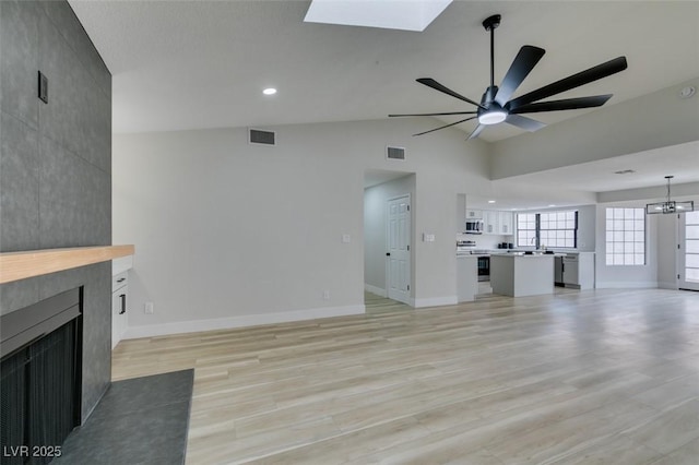 unfurnished living room with a tiled fireplace, vaulted ceiling with skylight, visible vents, and light wood-type flooring