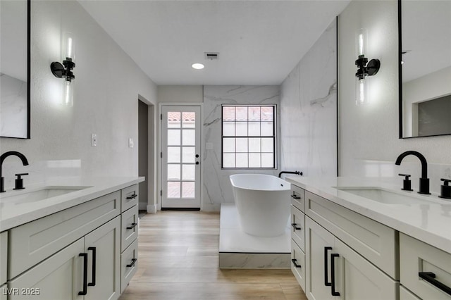 bathroom with a sink, a freestanding tub, two vanities, and wood finished floors