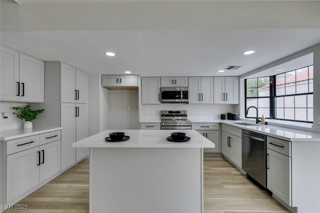 kitchen with a kitchen island, a sink, light countertops, appliances with stainless steel finishes, and light wood-type flooring