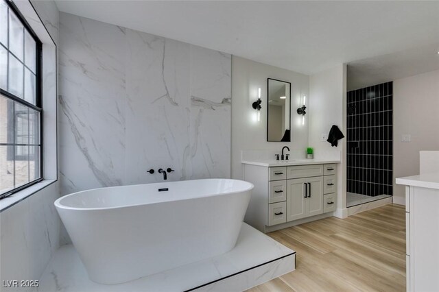 bathroom featuring a soaking tub, tile walls, wood finished floors, and vanity