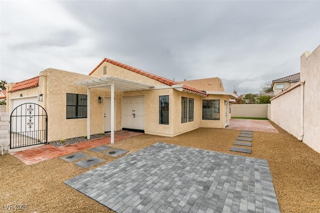 rear view of house featuring a gate, a fenced backyard, stucco siding, a tile roof, and a patio area