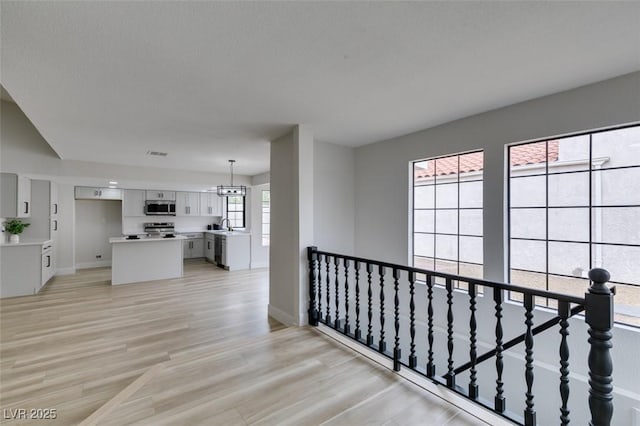 corridor featuring baseboards, visible vents, an inviting chandelier, light wood-style flooring, and a sink