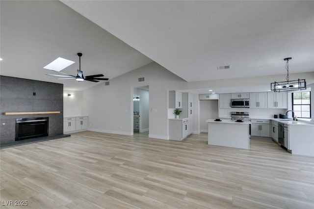 kitchen with light wood-style flooring, appliances with stainless steel finishes, a tiled fireplace, lofted ceiling with skylight, and open floor plan