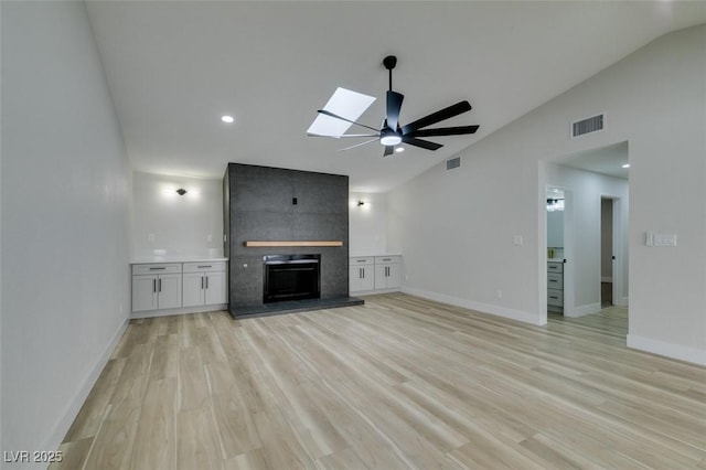 unfurnished living room with light wood-style floors, lofted ceiling with skylight, a fireplace, and visible vents