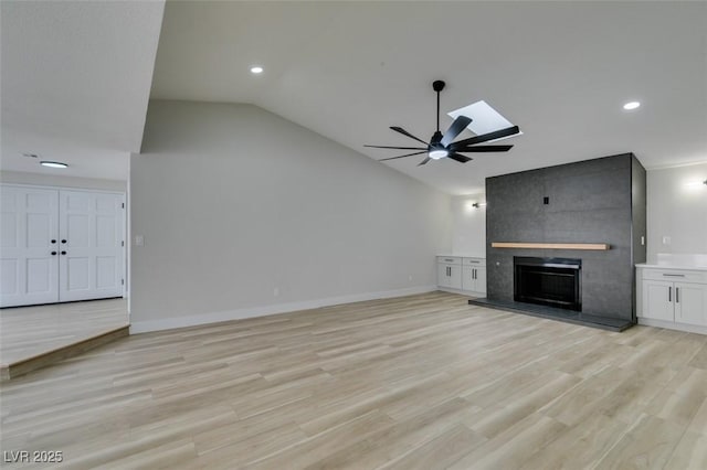 unfurnished living room featuring lofted ceiling, a ceiling fan, a large fireplace, light wood finished floors, and baseboards