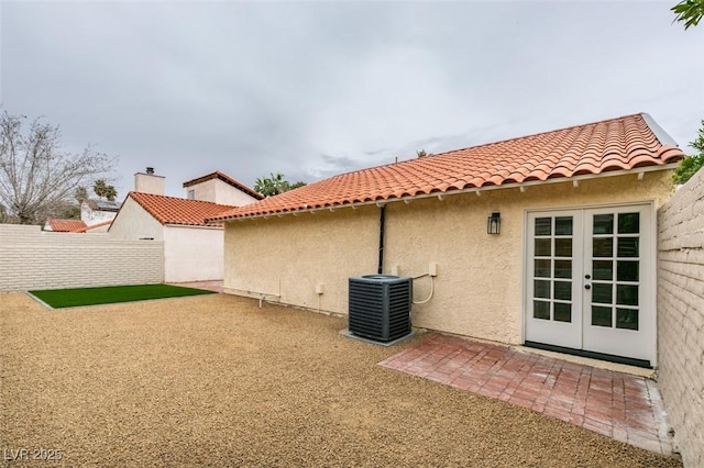 rear view of property with central air condition unit, stucco siding, fence, french doors, and a tiled roof