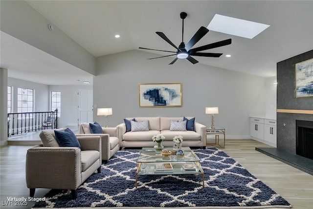 living room with baseboards, vaulted ceiling with skylight, recessed lighting, light wood-style flooring, and a fireplace