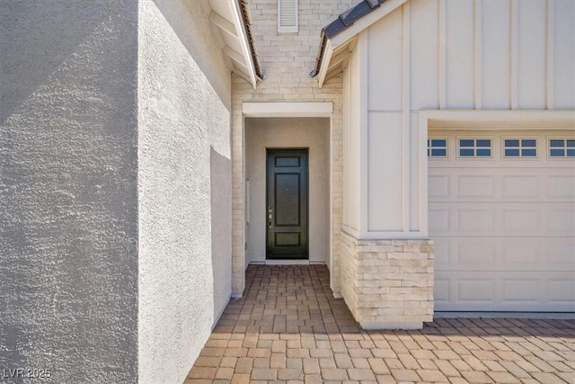 property entrance featuring a garage, stone siding, board and batten siding, and stucco siding