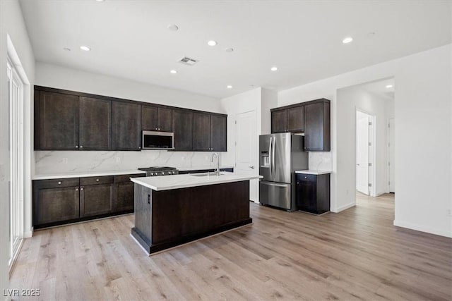 kitchen featuring stainless steel appliances, visible vents, a sink, dark brown cabinetry, and light wood-type flooring