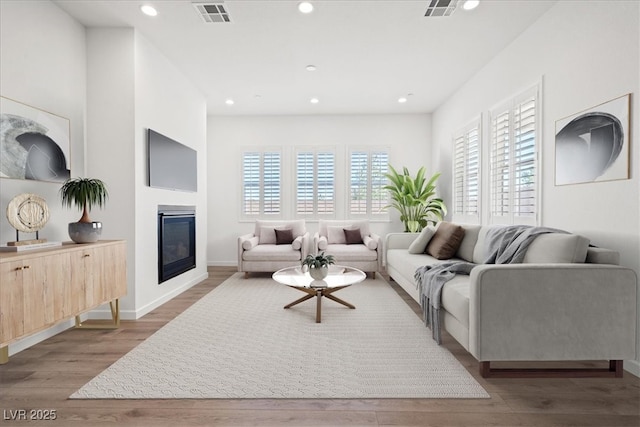 living area featuring baseboards, visible vents, a glass covered fireplace, wood finished floors, and recessed lighting