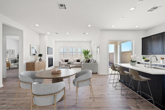 dining area featuring light wood-type flooring, a glass covered fireplace, visible vents, and recessed lighting